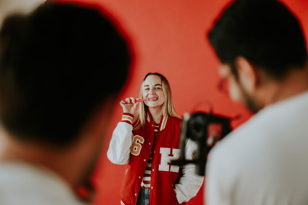 Cheerful woman brushing teeth during a photoshoot. Studio setting with vibrant red background.
